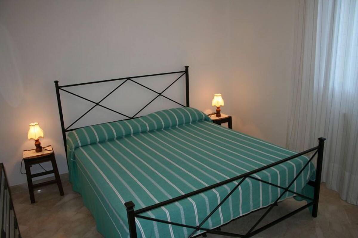 A single bed with a metal frame and a green striped bedspread, flanked by two bedside tables with lamps.