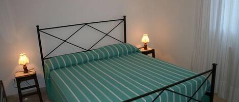 A single bed with a metal frame and a green striped bedspread, flanked by two bedside tables with lamps.