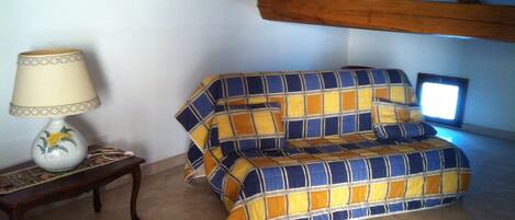 A room with a sofa covered in a plaid blanket, a small table with a lamp, and a television on a stand.