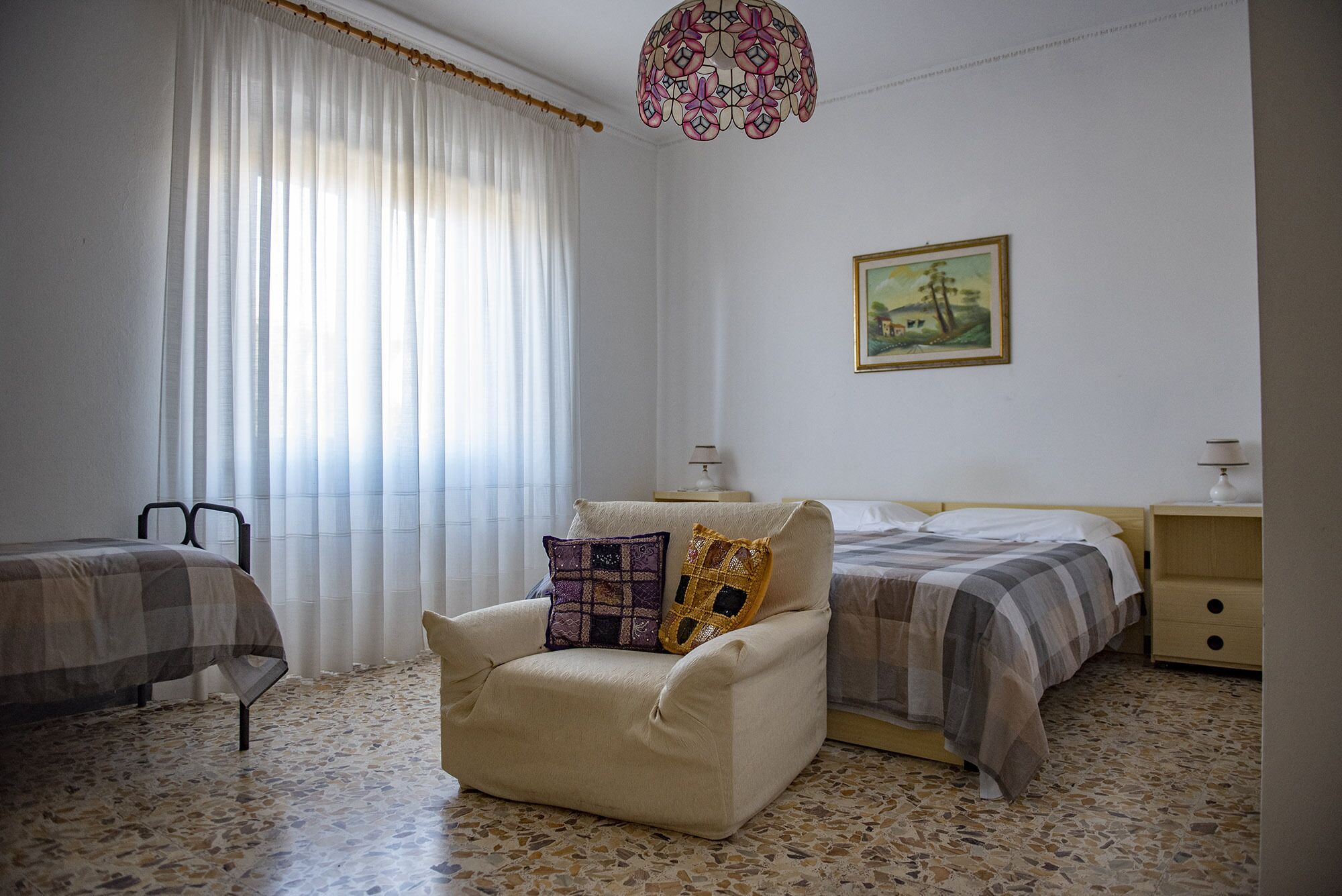 Une chambre à coucher avec un lit, une chaise, une table de chevet, une lampe et un tableau au mur.