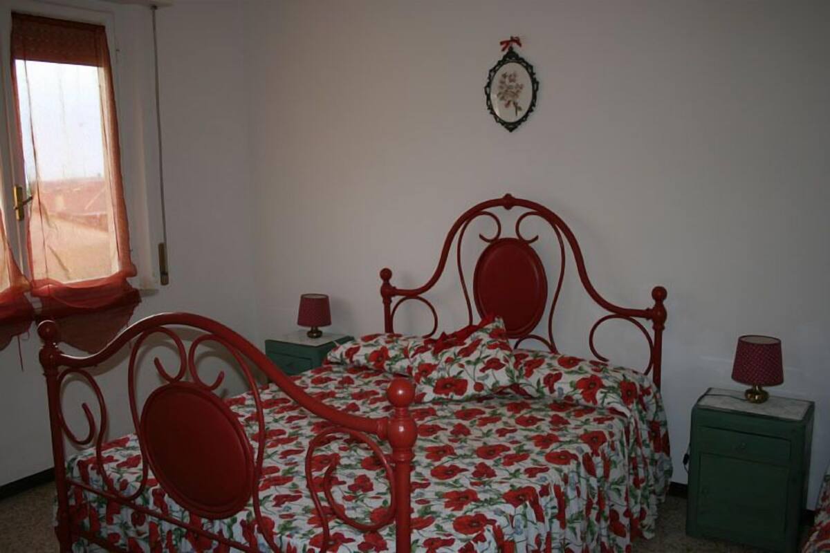 A bedroom with a red metal bed frame, floral bedding, two bedside tables with lamps, and a window with curtains.
