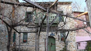 Un edificio de piedra con una puerta verde, plantas en macetas y una estructura de madera en la parte superior.