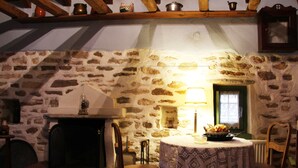 Una habitación rústica con pared de piedra, chimenea, mesa con mantel de encaje y sillas de madera.