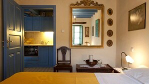 Una habitación con cama, escritorio, silla, espejo y kitchenette.