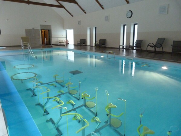 An indoor swimming pool with exercise equipment, chairs, and a clock on the wall.