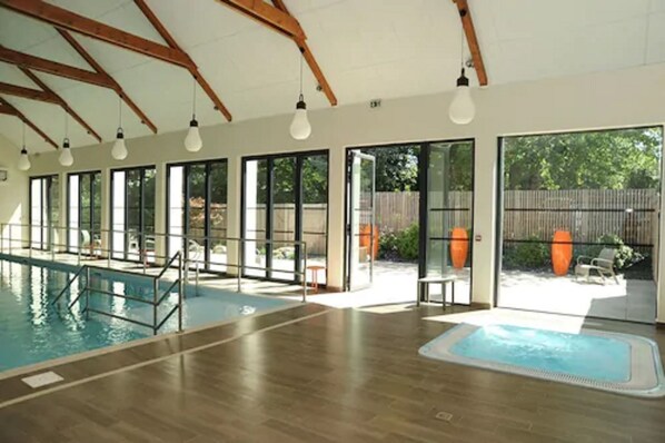 An indoor swimming pool with a wooden floor, large windows, and a view of the outside. - Loire & Sens (Les Garennes-sur-Loire)