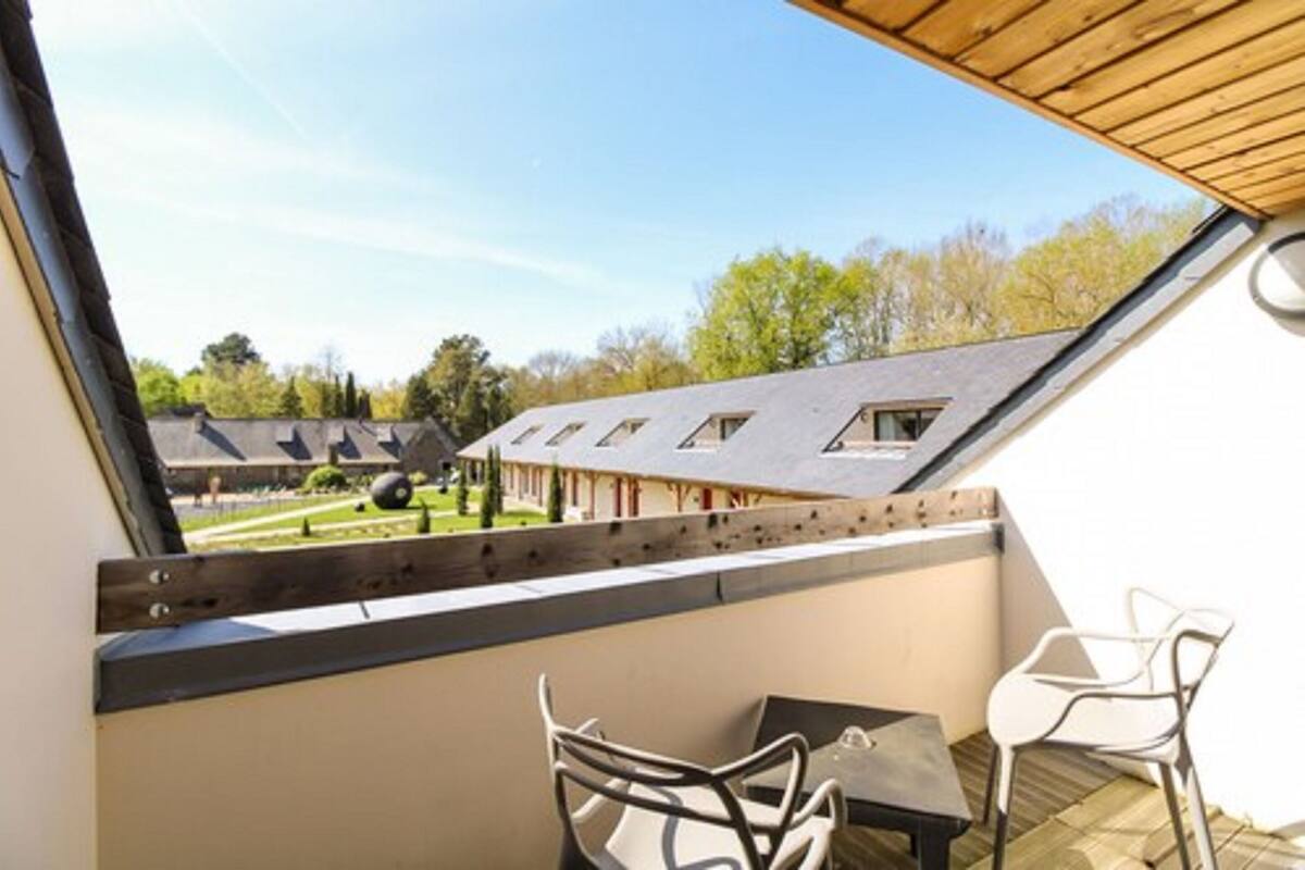 A balcony with a view of a building with multiple roofs, a table, and two chairs.