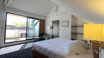 A hotel room with a bed, a desk, a chair, a window, and a door.