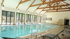 An indoor swimming pool with clear windows, wooden beams, and lounge chairs. - Loire & Sens (Les Garennes-sur-Loire)