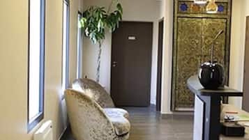 Un pasillo con una silla, una planta, una puerta y una mesa de recepción.