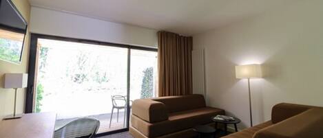 Habitación de hotel con sofá, una mesita, una lámpara y vistas al exterior.