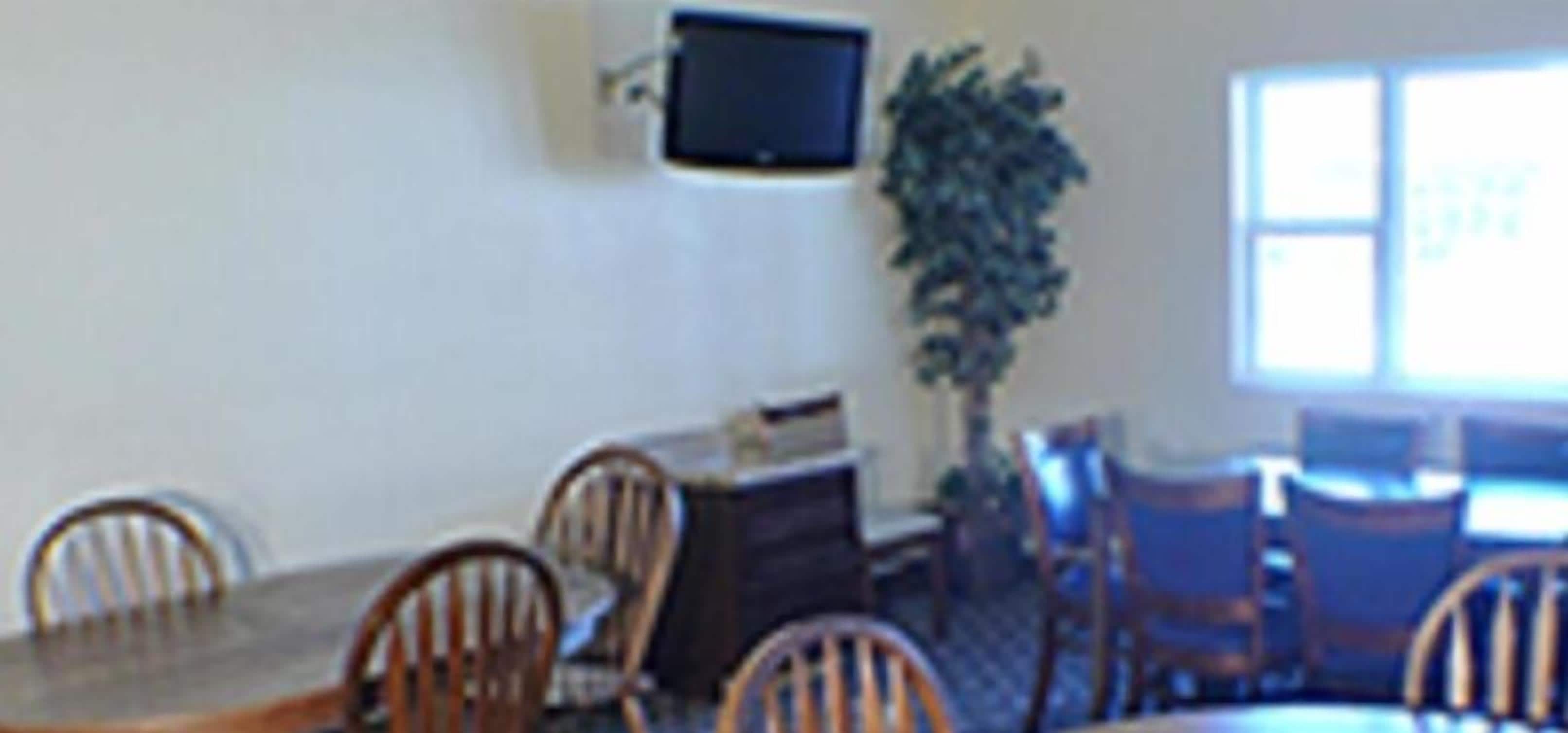 A dining area with a table and chairs, a television mounted on the wall, and a potted plant.