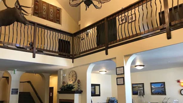 A hotel lobby with a staircase, a fireplace, and a dining area with tables and chairs. - Blue Spruce Inn (Meeker)