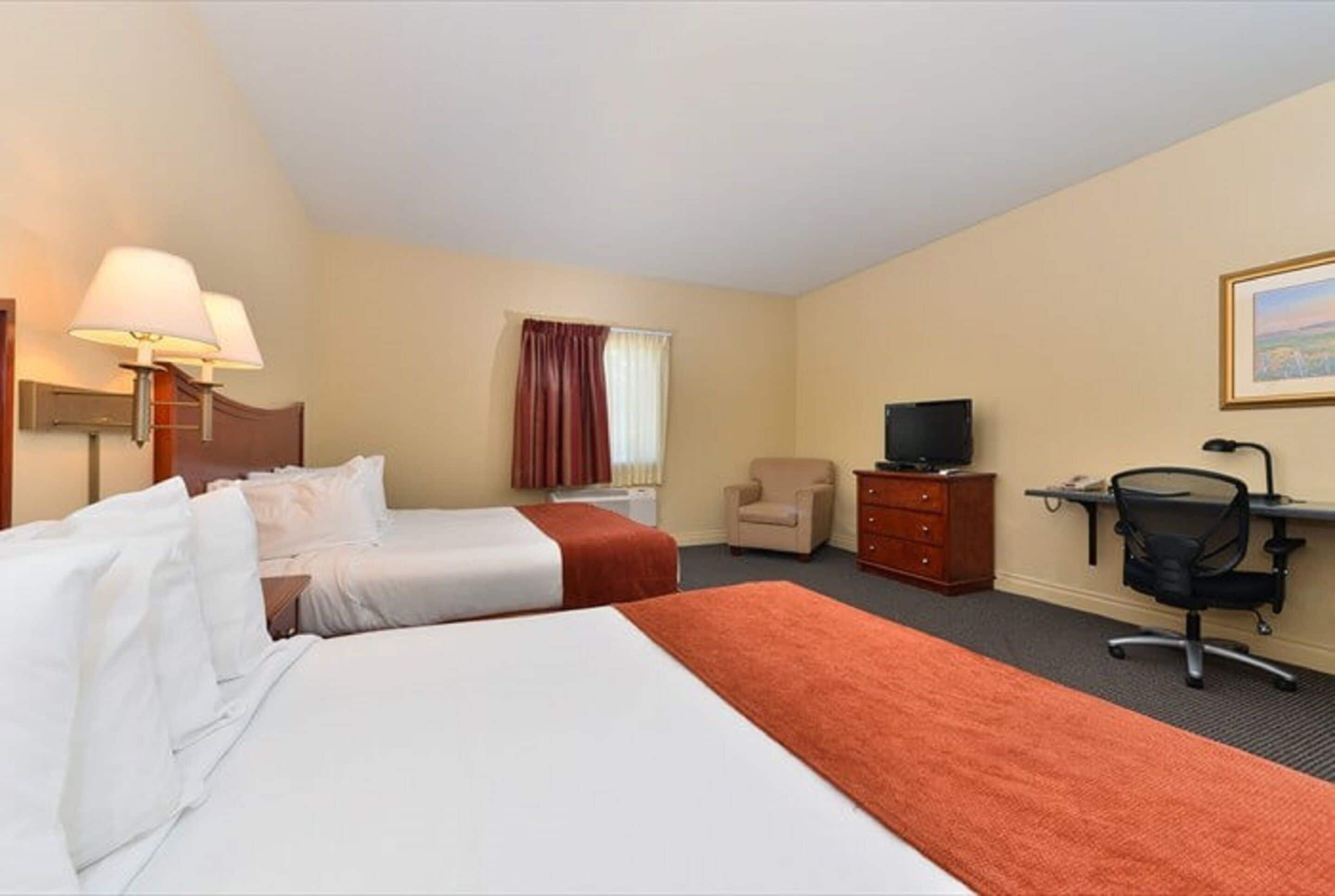Une chambre d’hôtel avec deux lits, un bureau, une chaise, une télévision et une fenêtre avec des rideaux.
