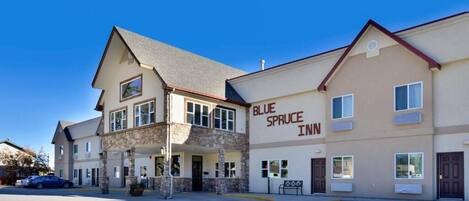 Un hôtel de deux étages, le Blue Spruce Inn, avec une façade en pierre, de grandes fenêtres et un ciel d’un bleu éclatant.