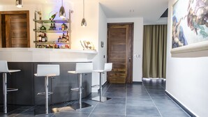 A modern kitchen with a bar area, including a counter with stools, shelves with bottles, and a wooden door. - Paramount Bay Penthouse (Birzebbuga)