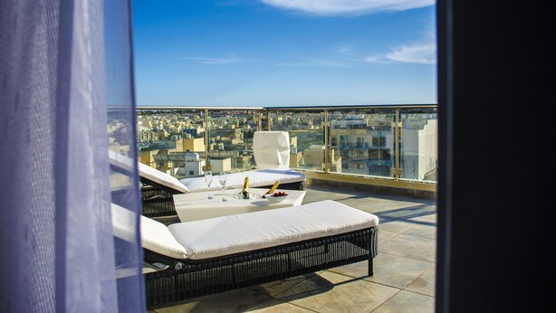 A rooftop terrace with two lounge chairs, a table with a bottle and glasses, and a city view. - Paramount Bay Penthouse (Birzebbuga)