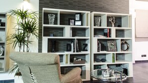 A modern living room with a grey armchair, a glass coffee table, and a white bookshelf filled with books and decorative items. - Paramount Bay Penthouse (Birzebbuga)