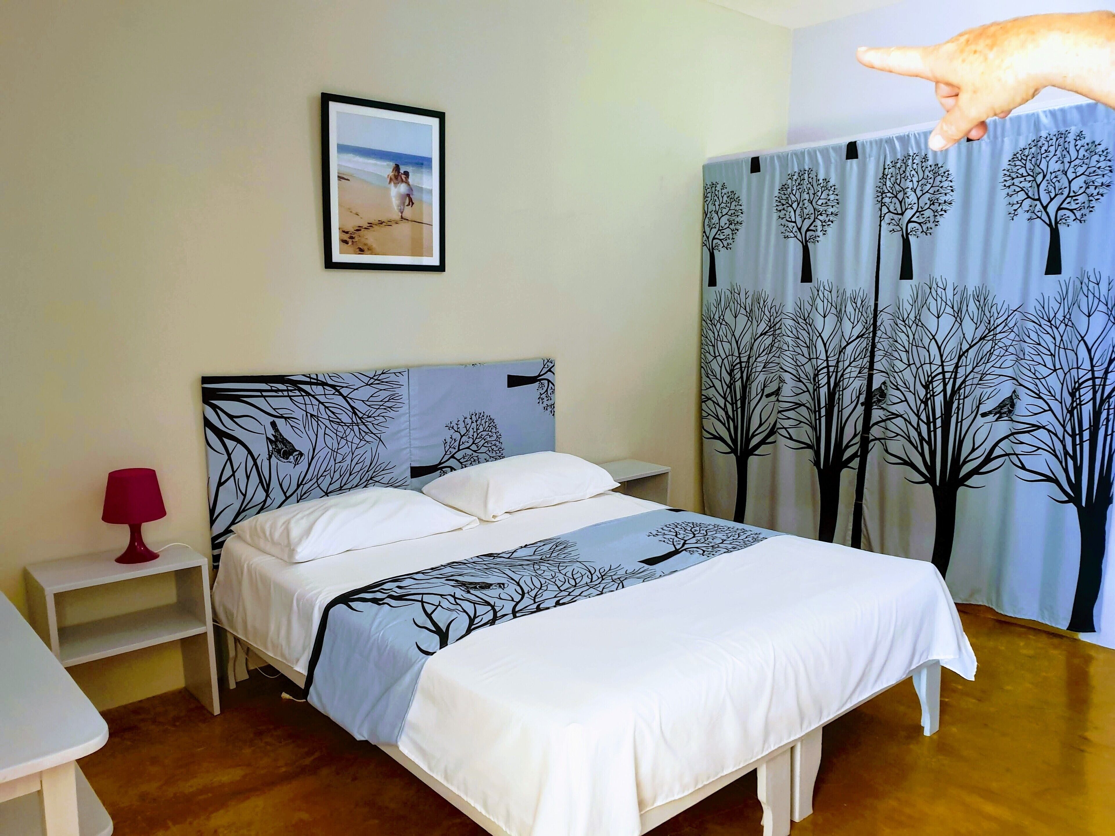 Ein ordentlich bezogenes Bett mit einem Kopfstück im Baumdesign, einer Nachttischlampe und einem gerahmten Bild an der Wand.
