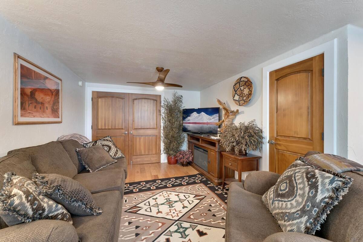 A living room with a brown sofa, patterned cushions, a wooden cabinet, a television, and a ceiling fan.