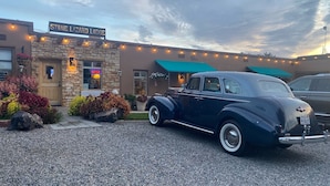 A vintage car parked in front of Stone Lizard Lodge, a building with a stone facade and string lights.