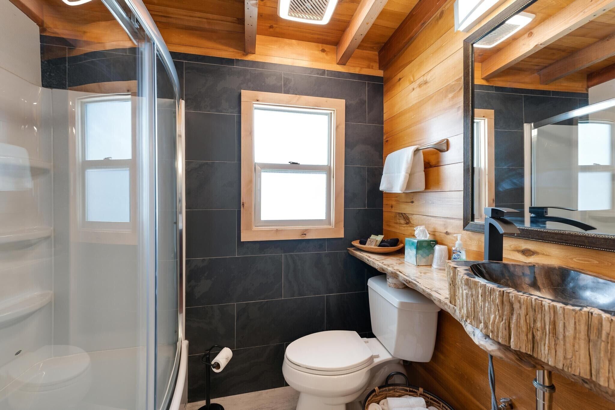 Ein modernes Badezimmer mit Duschkabine aus Glas, einer weißen Toilette, einem Holzwaschtisch mit Waschbecken und einem großen Spiegel.
