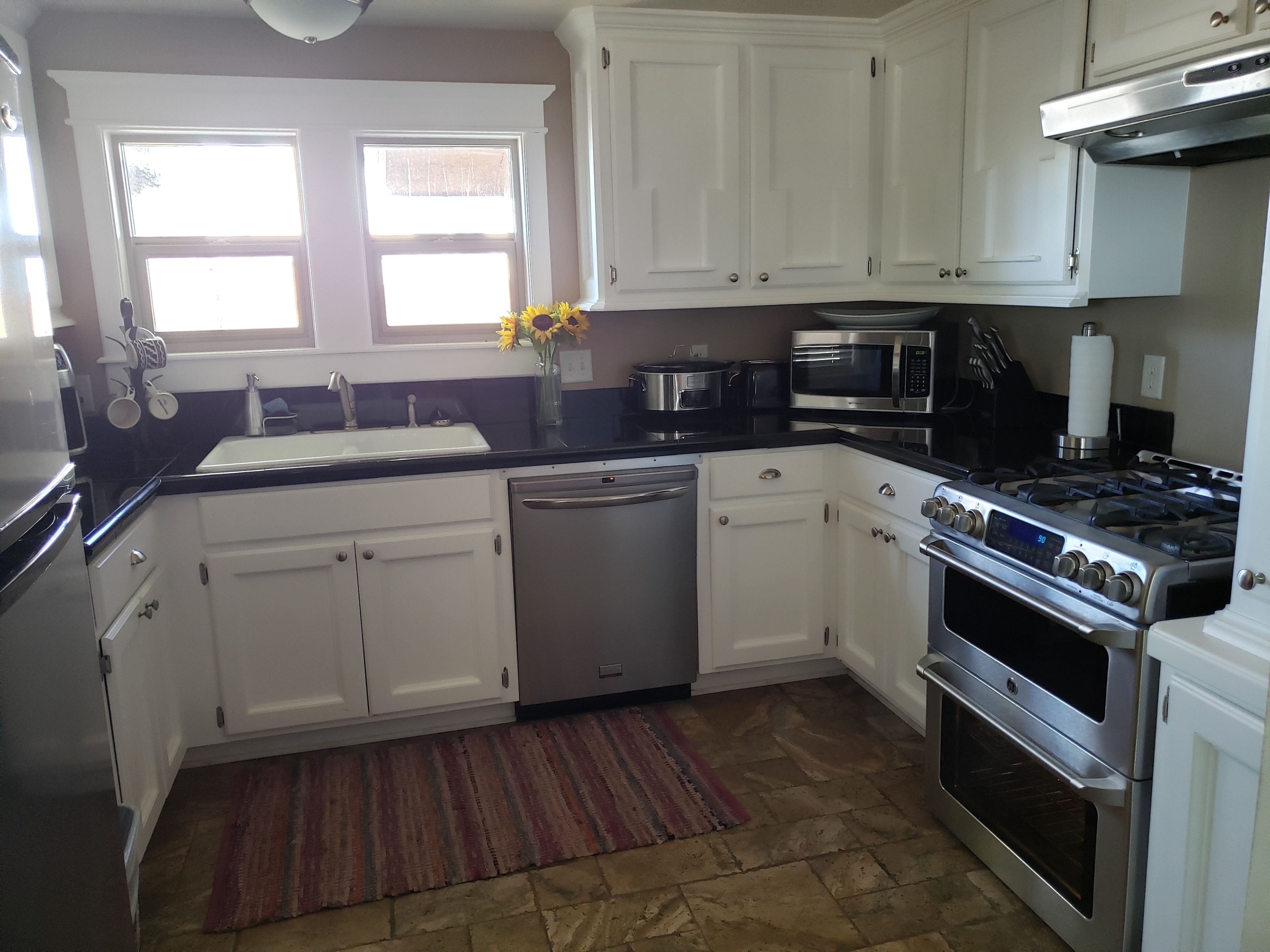 A modern kitchen with white cabinets, stainless steel appliances, a dishwasher, a stove, and a microwave.