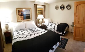 A hotel room with two beds, a nightstand, a lamp, a framed picture, a wooden door, and three wall decorations.