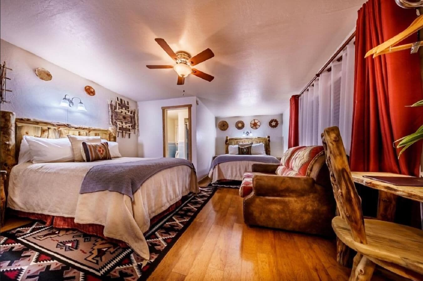 A cozy bedroom with a wooden bed, a chair, a small table, and a ceiling fan.