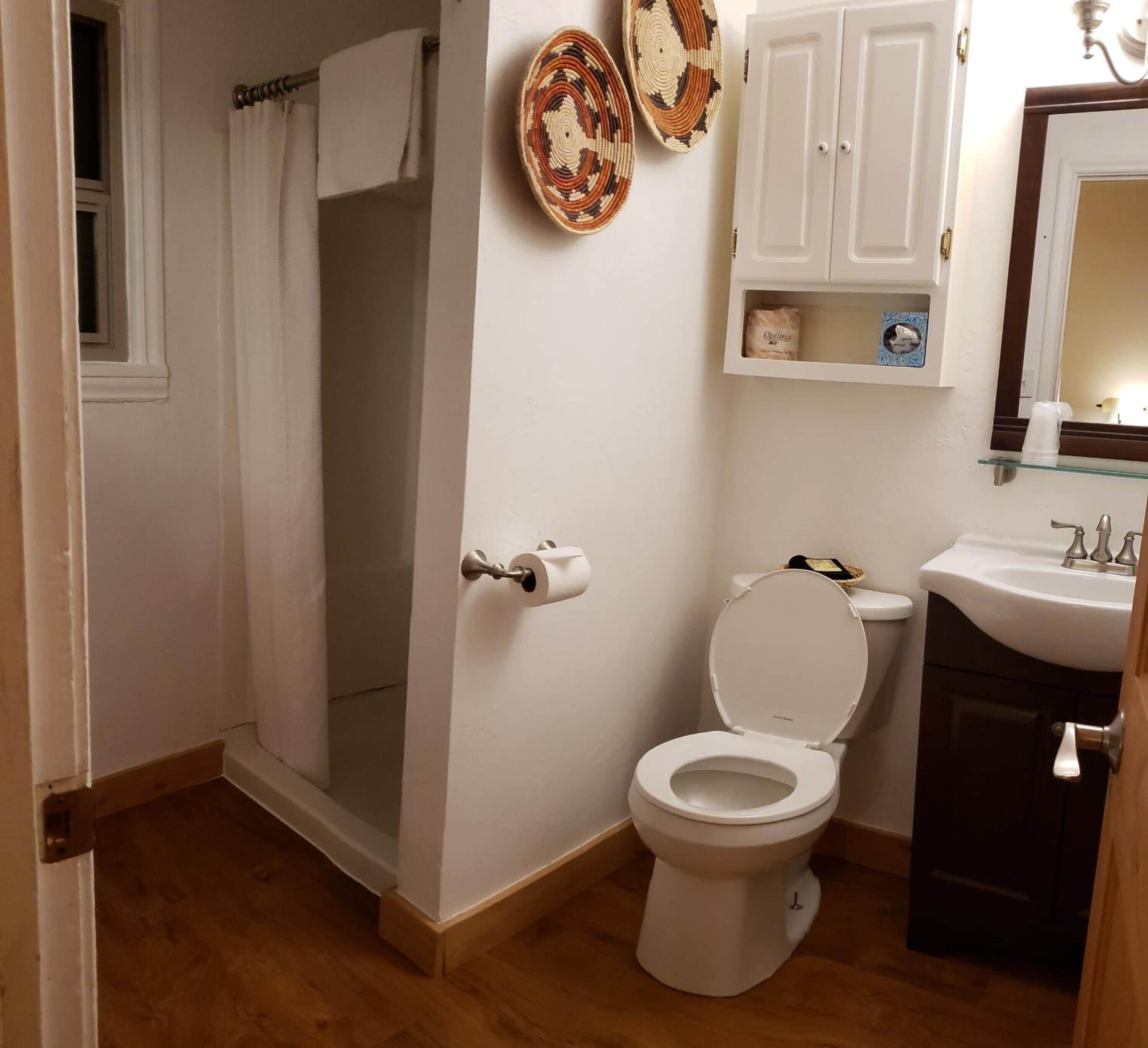 Une salle de bain avec des toilettes, un lavabo et une douche. On y trouve des paniers en osier accrochés au mur et un meuble au-dessus du lavabo.