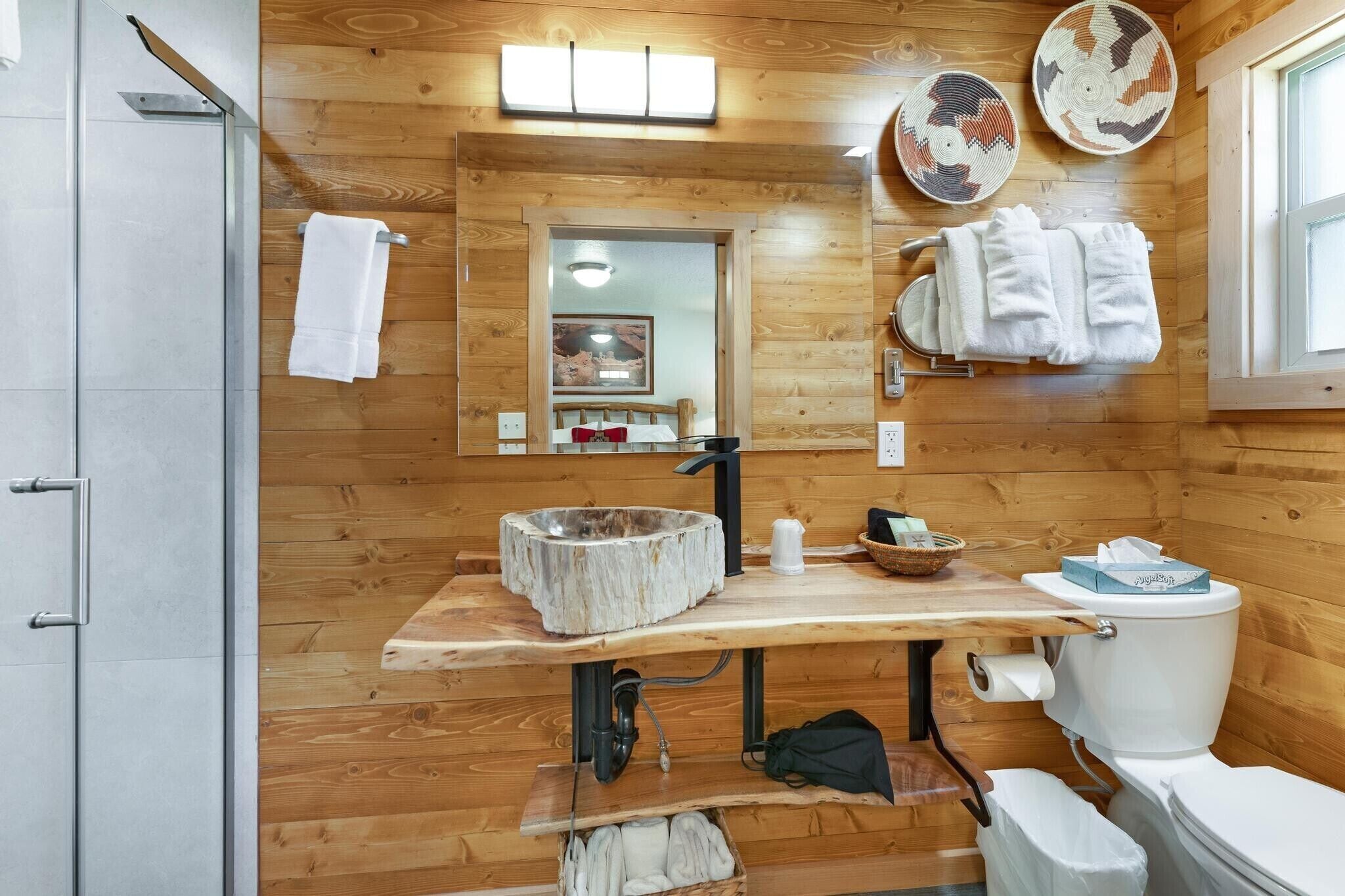 Une salle de bain aux murs lambrissés, avec un lavabo en pierre, un miroir et des toilettes.