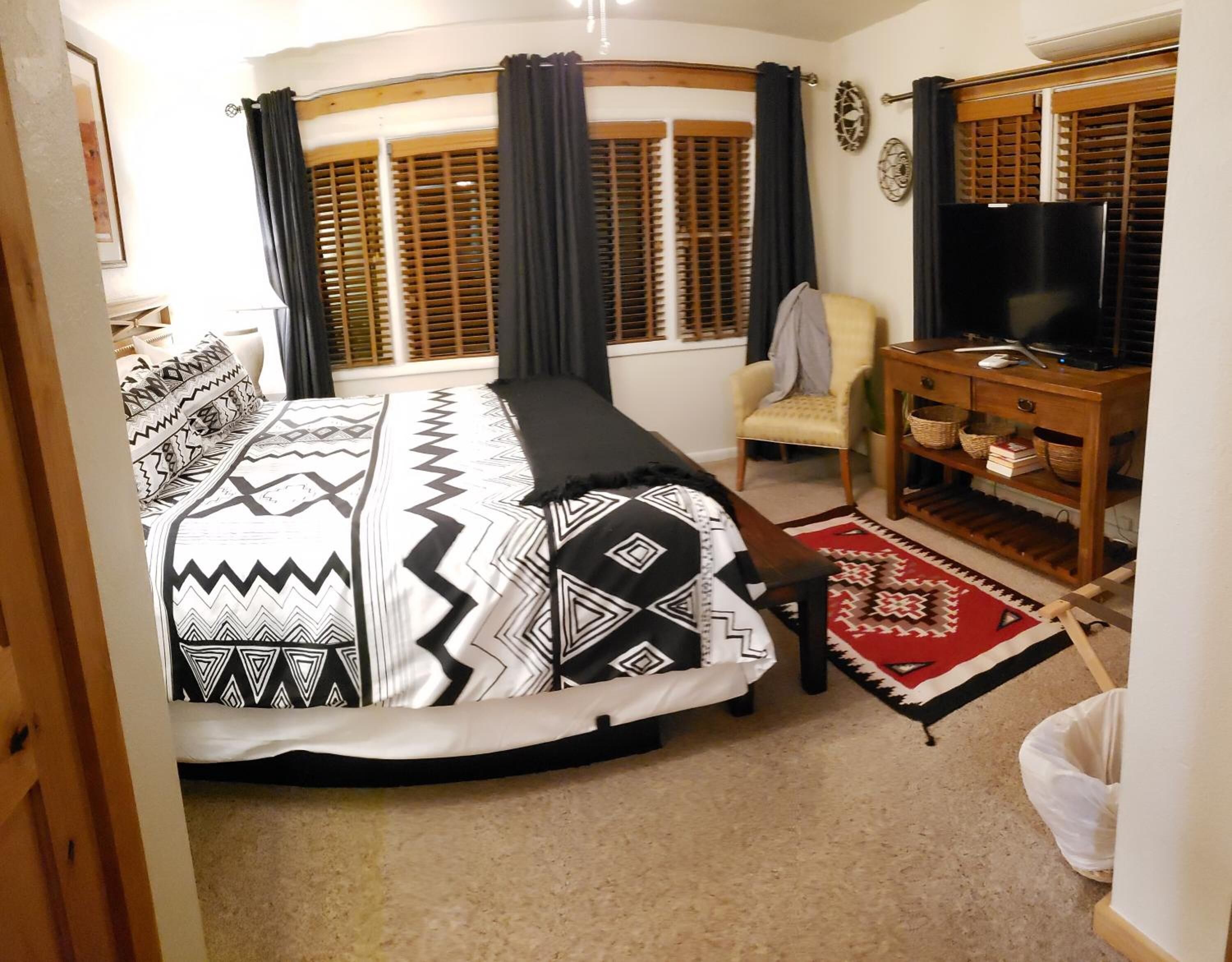 Un dormitorio con una cama, una silla, un televisor y un armario de madera.