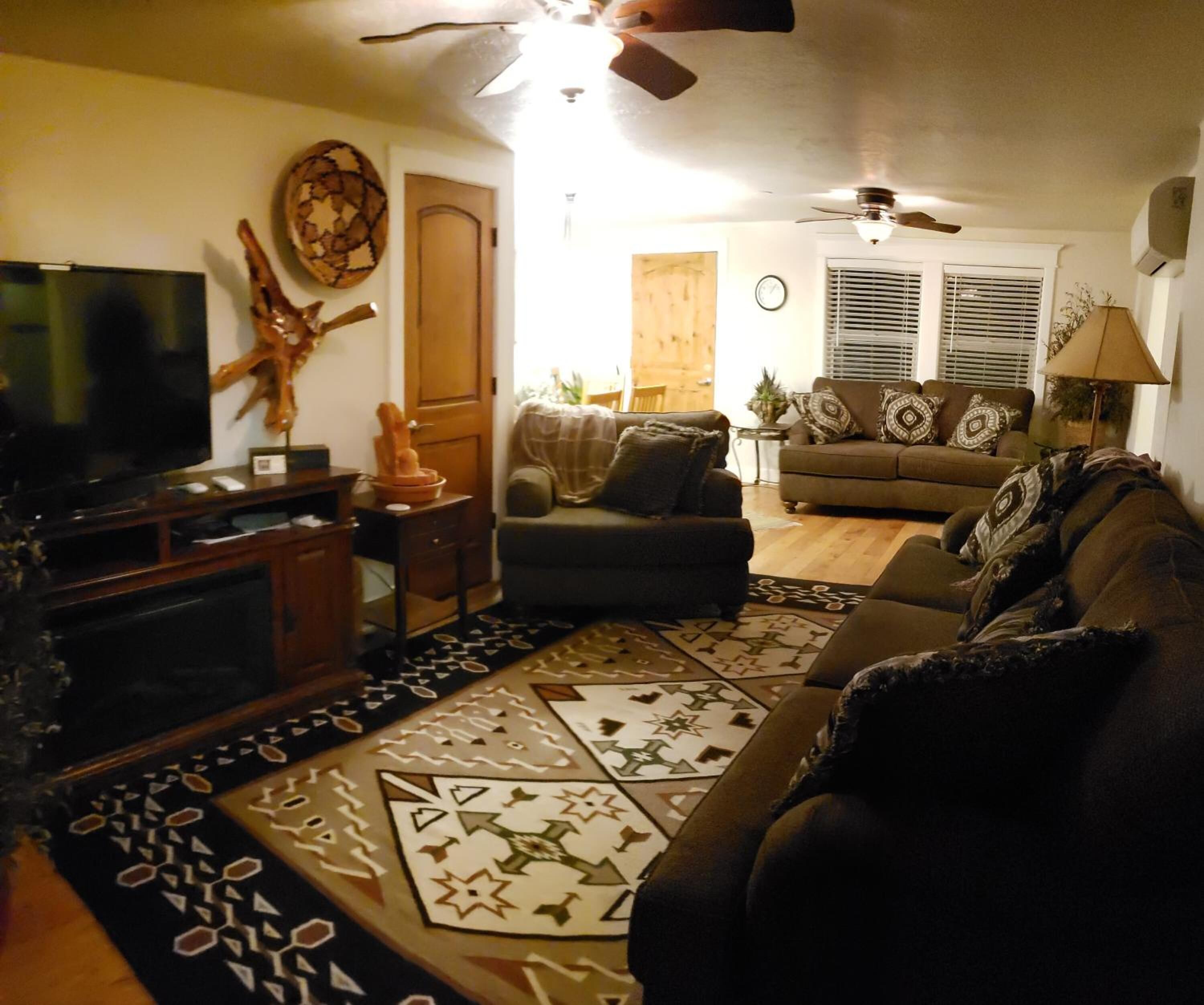 A living room with a television, a ceiling fan, a sofa, and a patterned rug.
