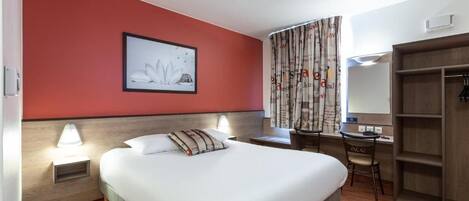 Habitación de hotel con cama, mesita de noche, lámpara, escritorio, silla, armario y un cuadro en la pared.