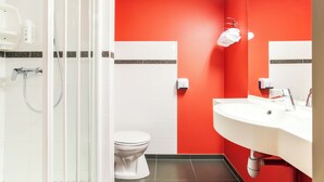 Une salle de bain avec des toilettes blanches, un lavabo avec un miroir et un espace douche.
