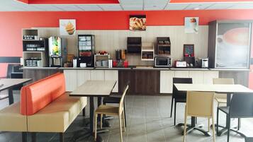 Interior de un restaurante de comida rápida con mesas, mostrador y diverso equipo para servicio de alimentos.