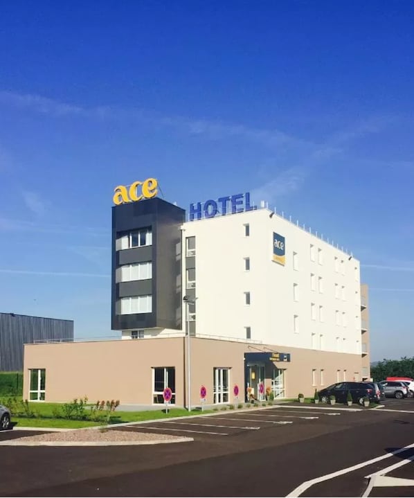 A modern hotel with a prominent 'ace' sign on the top left, a flat facade, and a parking lot in front. - ACE Hôtel Creutzwald St Avold (Creutzwald)