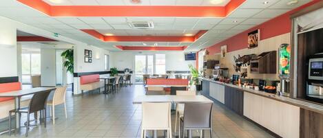 A modern restaurant with a central dining area, booths, and a counter with a beverage station.