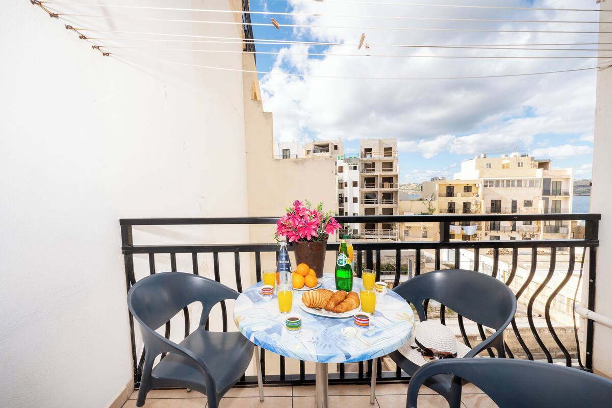 Un balcón con una mesa lista para el desayuno, que incluye cruasanes, jugo de naranja y una botella de agua.
