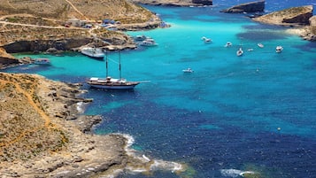 A coastal area with boats anchored near rocky shores, clear turquoise waters, and a small beach with people.