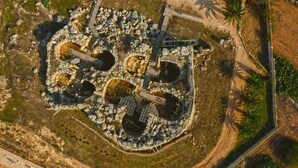 Vista aérea de un sitio histórico con ruinas, senderos y un puente de madera.
