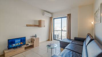 A modern living room with a flat-screen TV, a glass coffee table, a sofa, and a balcony with a view.