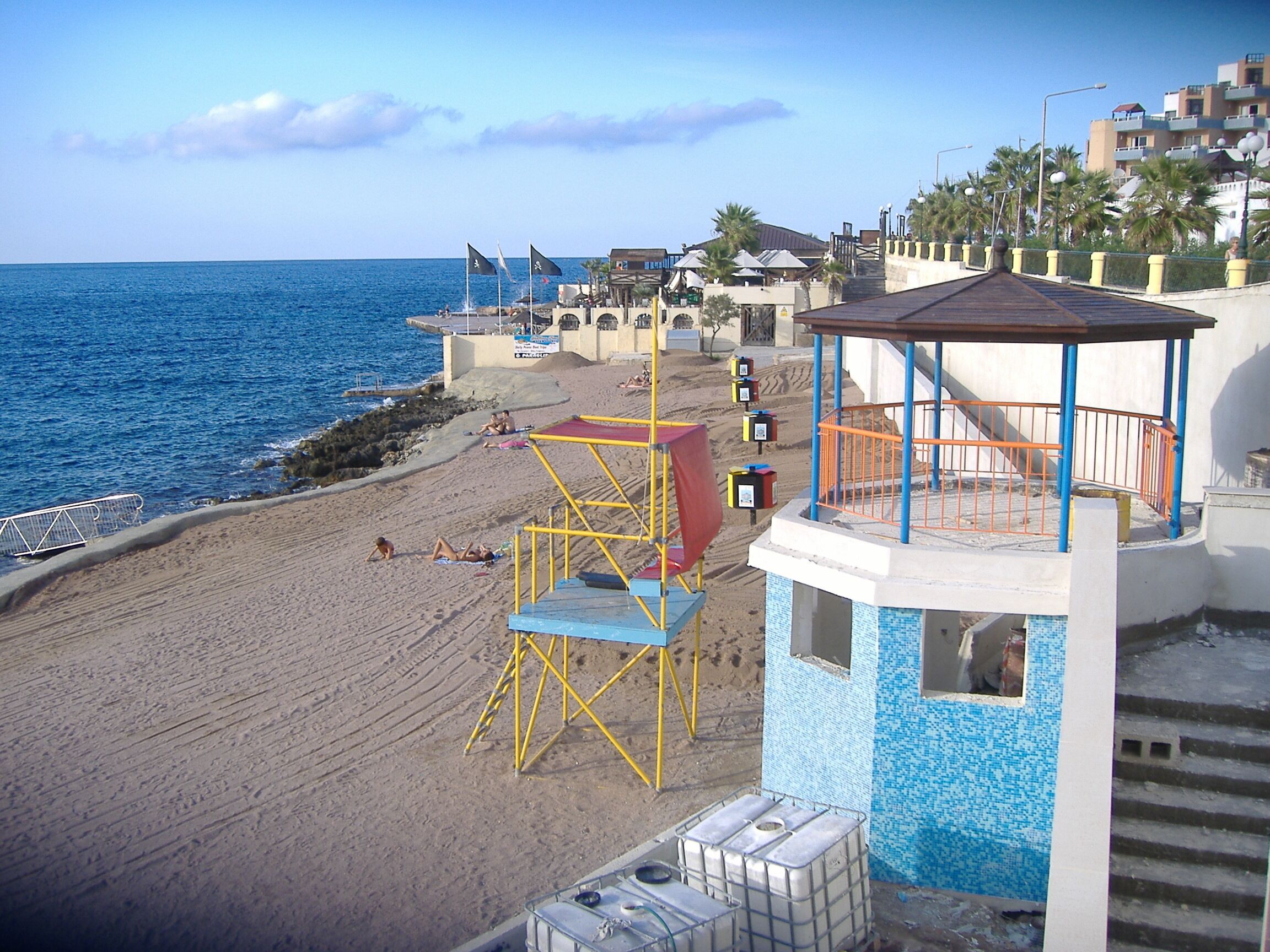 A beach with a lifeguard tower, palm trees, and a clear blue sky.