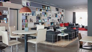A modern library with bookshelves, comfortable seating, and a dining area. - Living Hotel Frankfurt (Frankfurt)