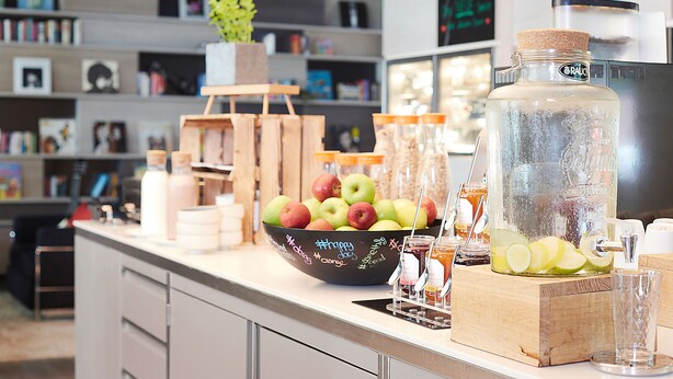 A kitchen counter with a bowl of apples, jars of honey, and a large water dispenser. - Living Hotel Frankfurt (Frankfurt)