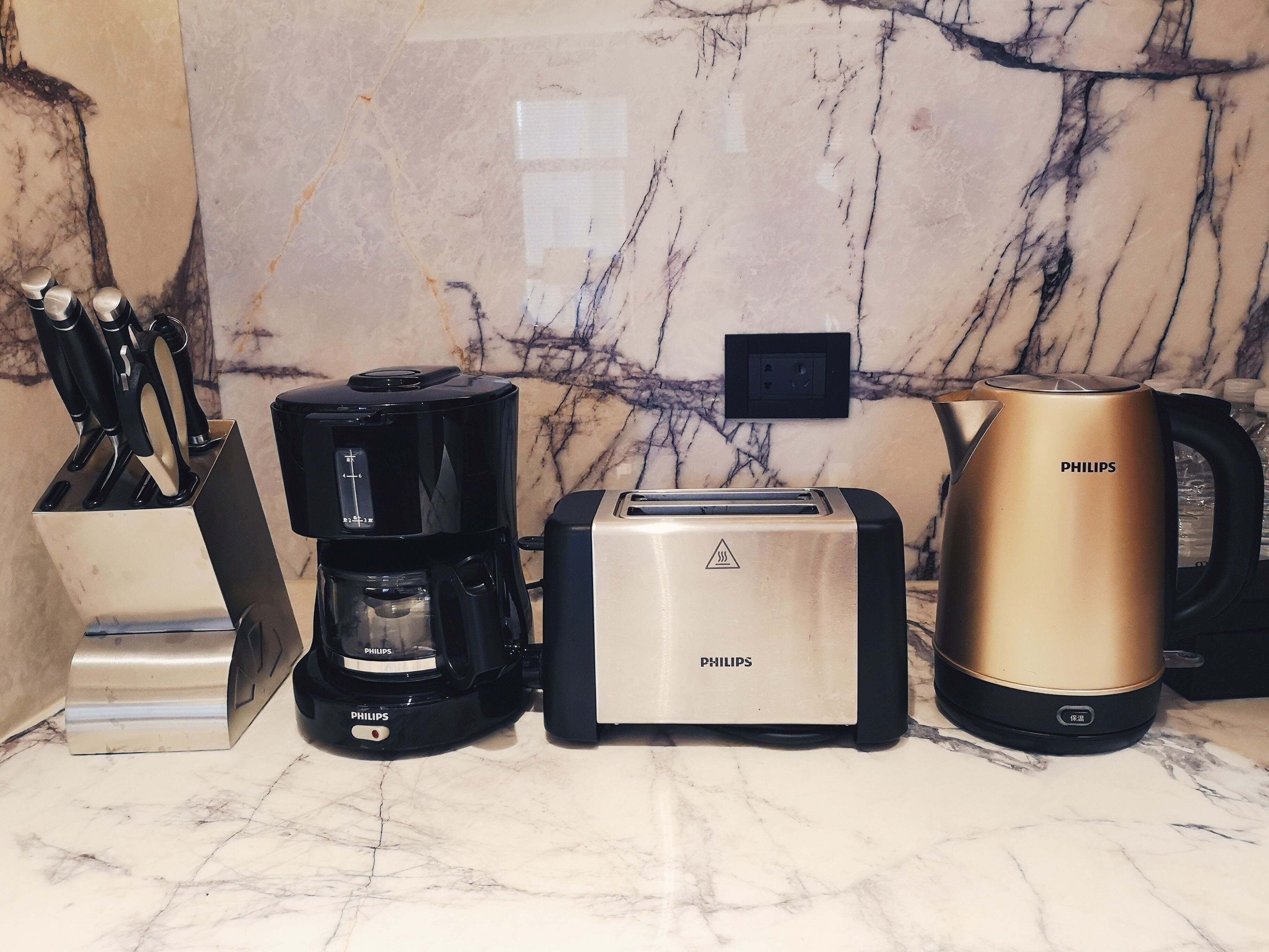 A kitchen counter with a coffee maker, toaster, and kettle, all branded Philips, against a marble backsplash.