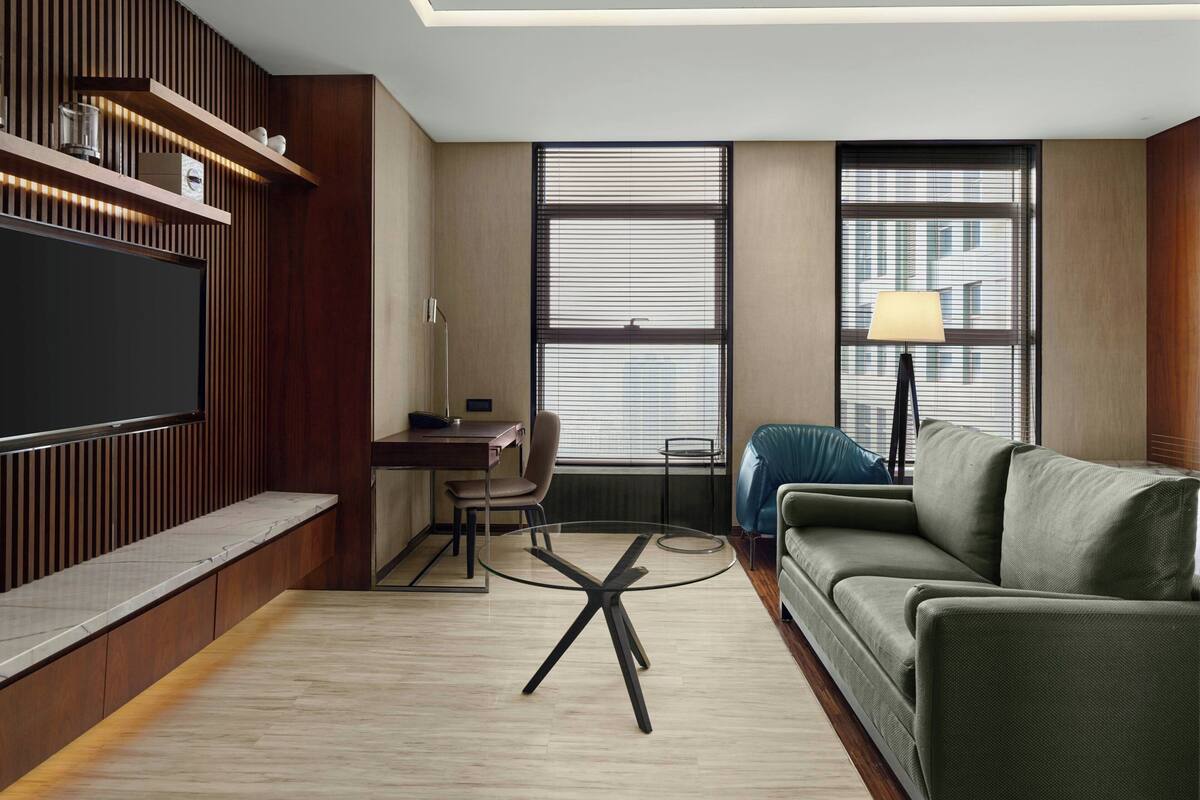 A modern living room with a flat-screen TV, a glass coffee table, a sofa, and a desk with a chair.