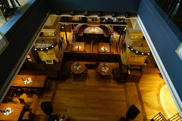 A restaurant with multiple tables and chairs, wooden flooring, and hanging light fixtures.