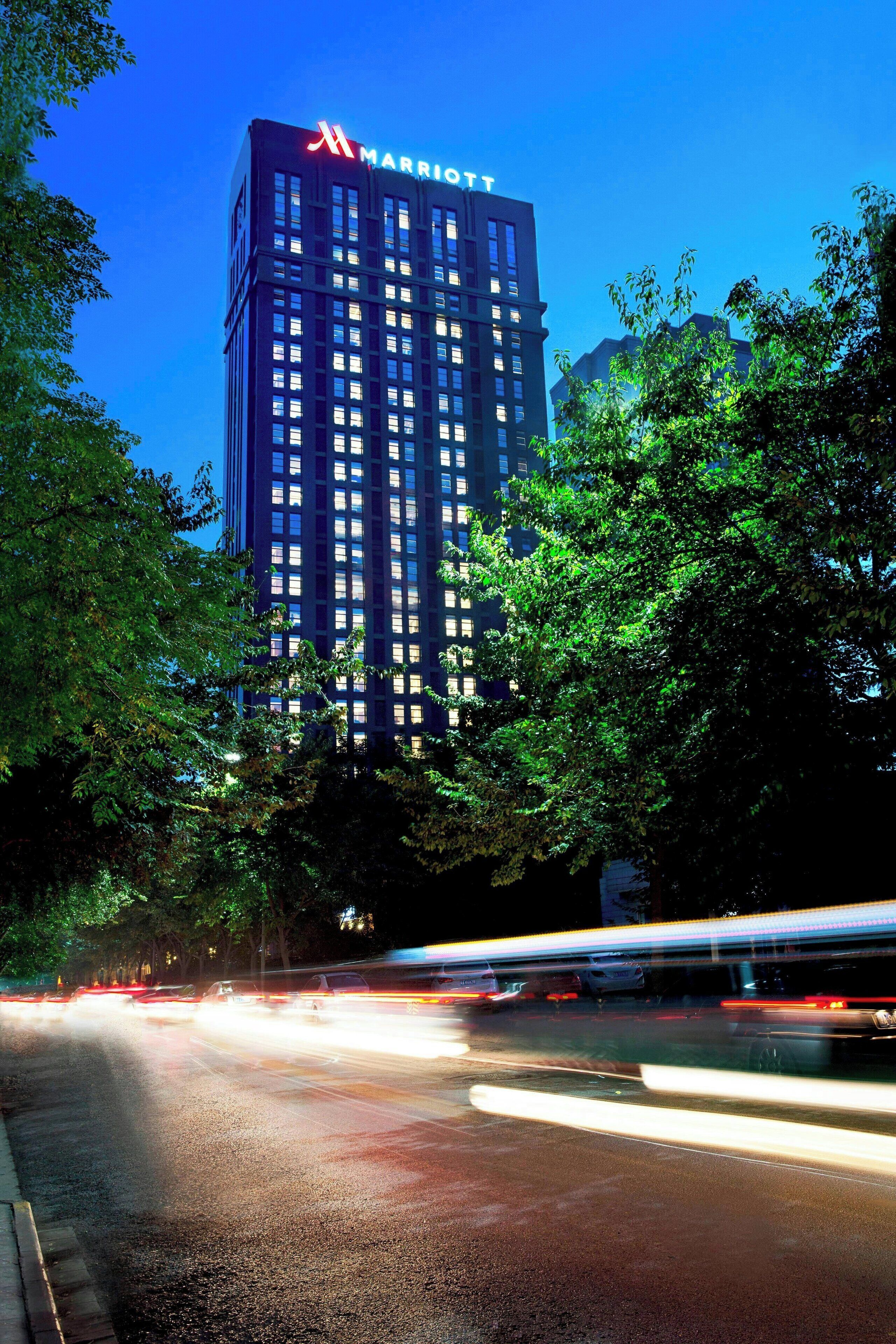 A Marriott hotel building with a modern design, surrounded by trees and a busy street with moving vehicles.