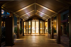 A hotel entrance with a modern design, featuring a prominent marquee sign above the doors and a covered walkway leading to the entrance.